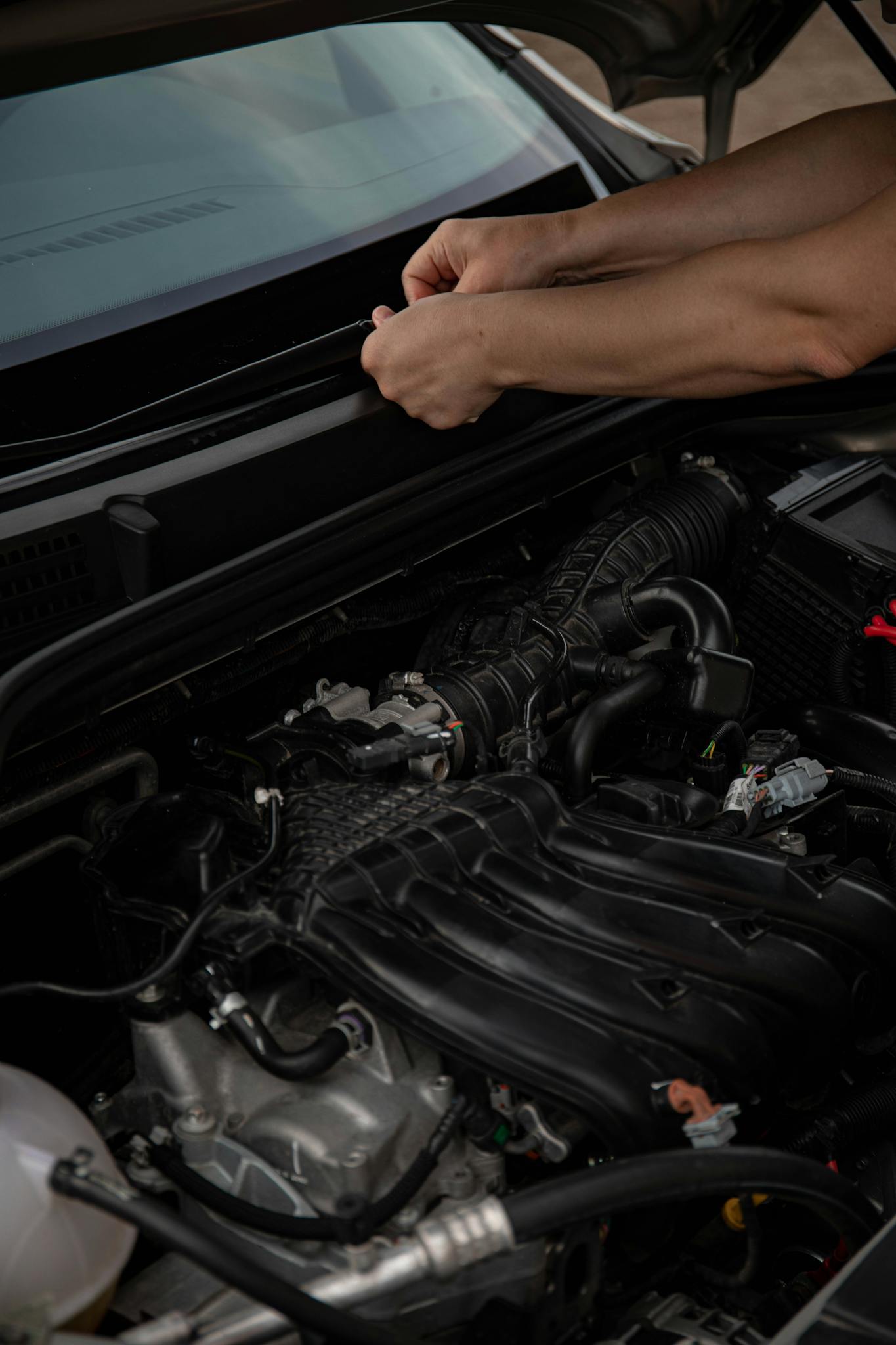 Close-up of hands working on a car engine, showcasing automotive maintenance.